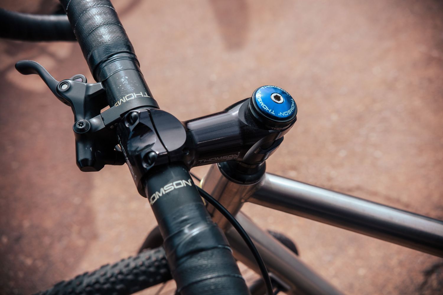 Close-up of a black Thomson bicycle stem and handlebars with a blue anodized top cap on a road bike.