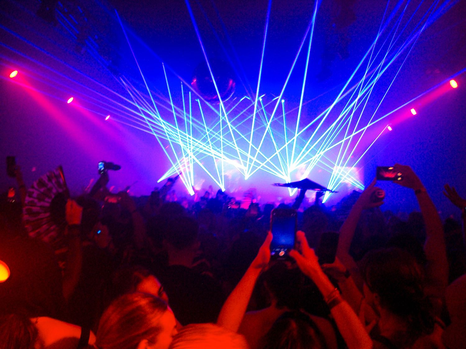 Crowd at a concert with vibrant blue and pink laser light show illuminating the dark venue.