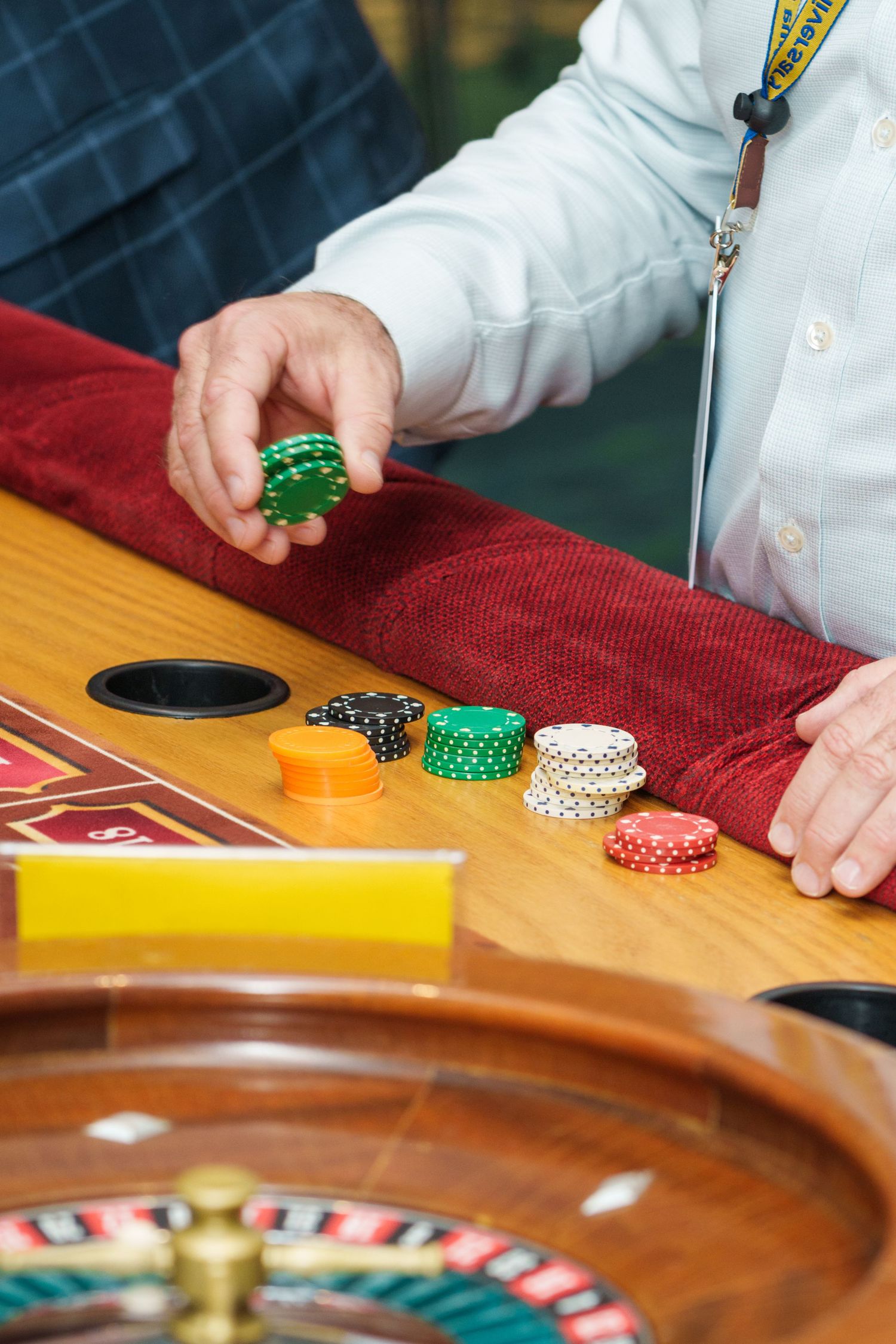 Casino dealer handling green chips at a roulette table with colorful betting chips stacked on red velvet surface.