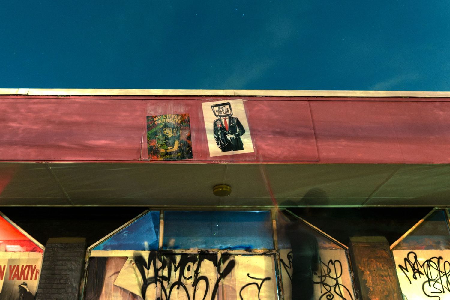 Graffiti-covered building exterior with street art posters under a vivid blue sky at dusk.