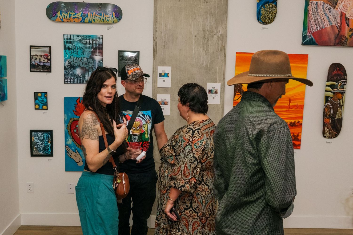 Group of art enthusiasts socializing at a street art gallery opening surrounded by colorful paintings and skateboard decks.