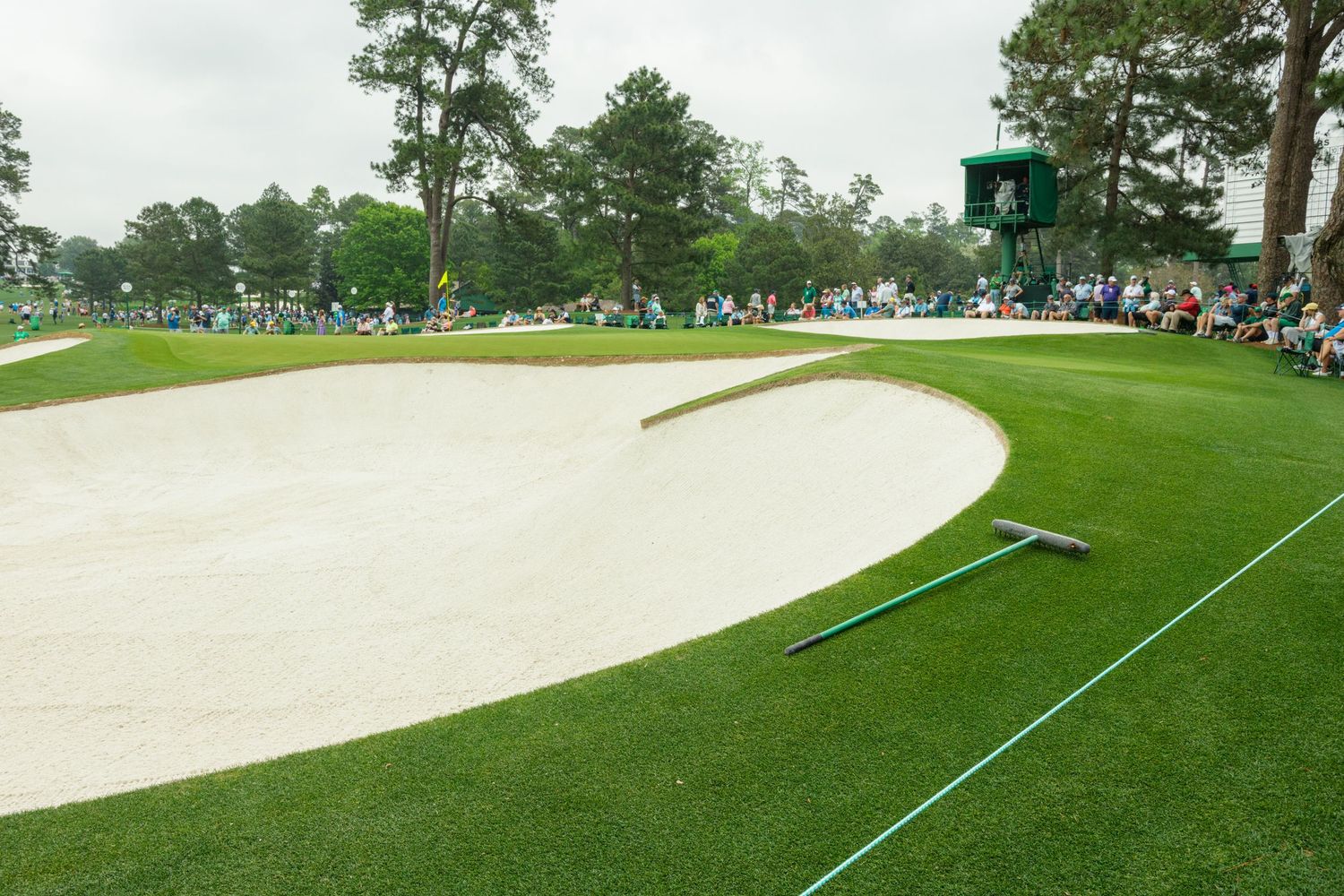 A pristine sand bunker on a lush golf course fairway with spectators and green scoreboard in background.