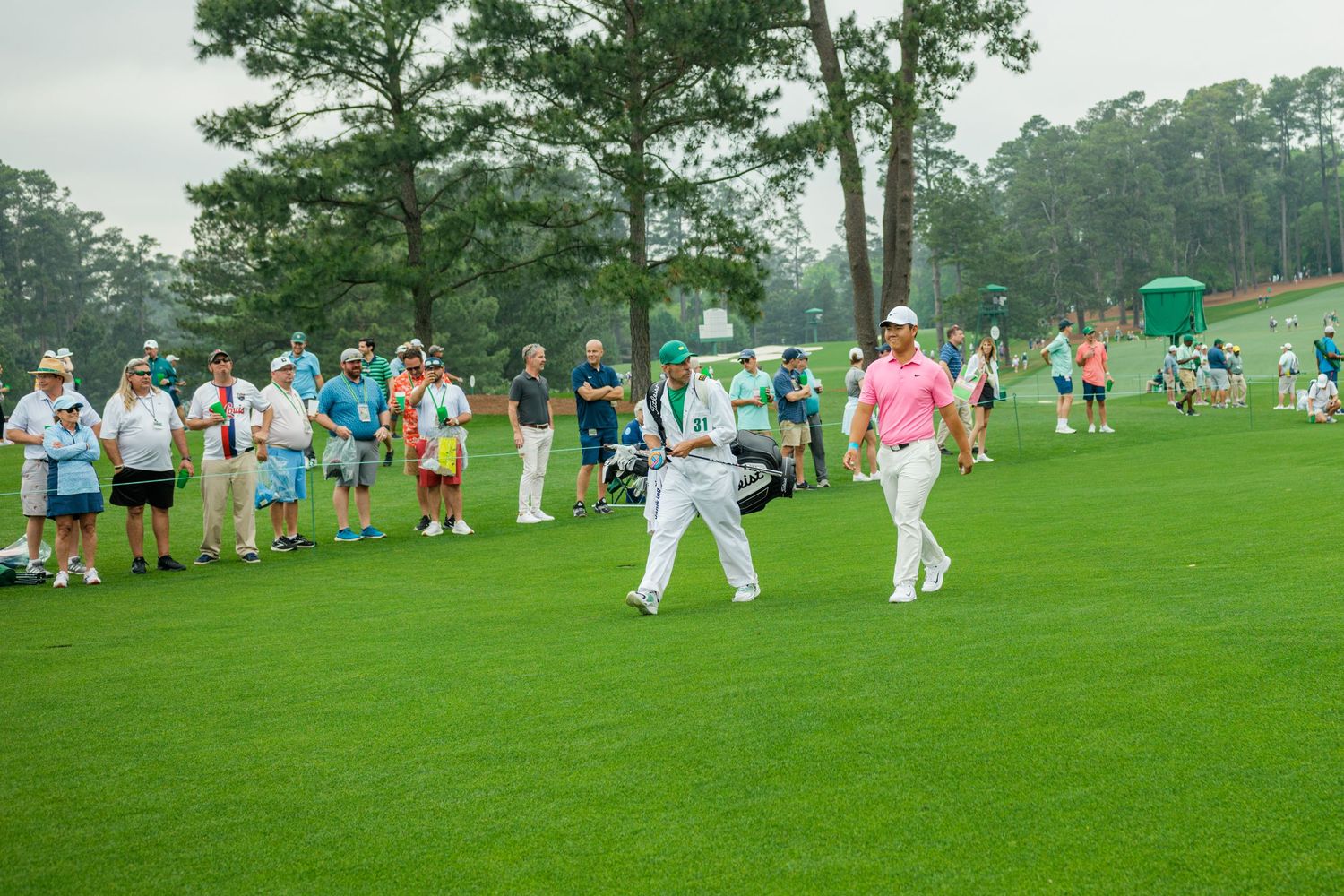 Golfer in pink shirt walks fairway with caddie at Augusta National golf course during Masters Tournament.