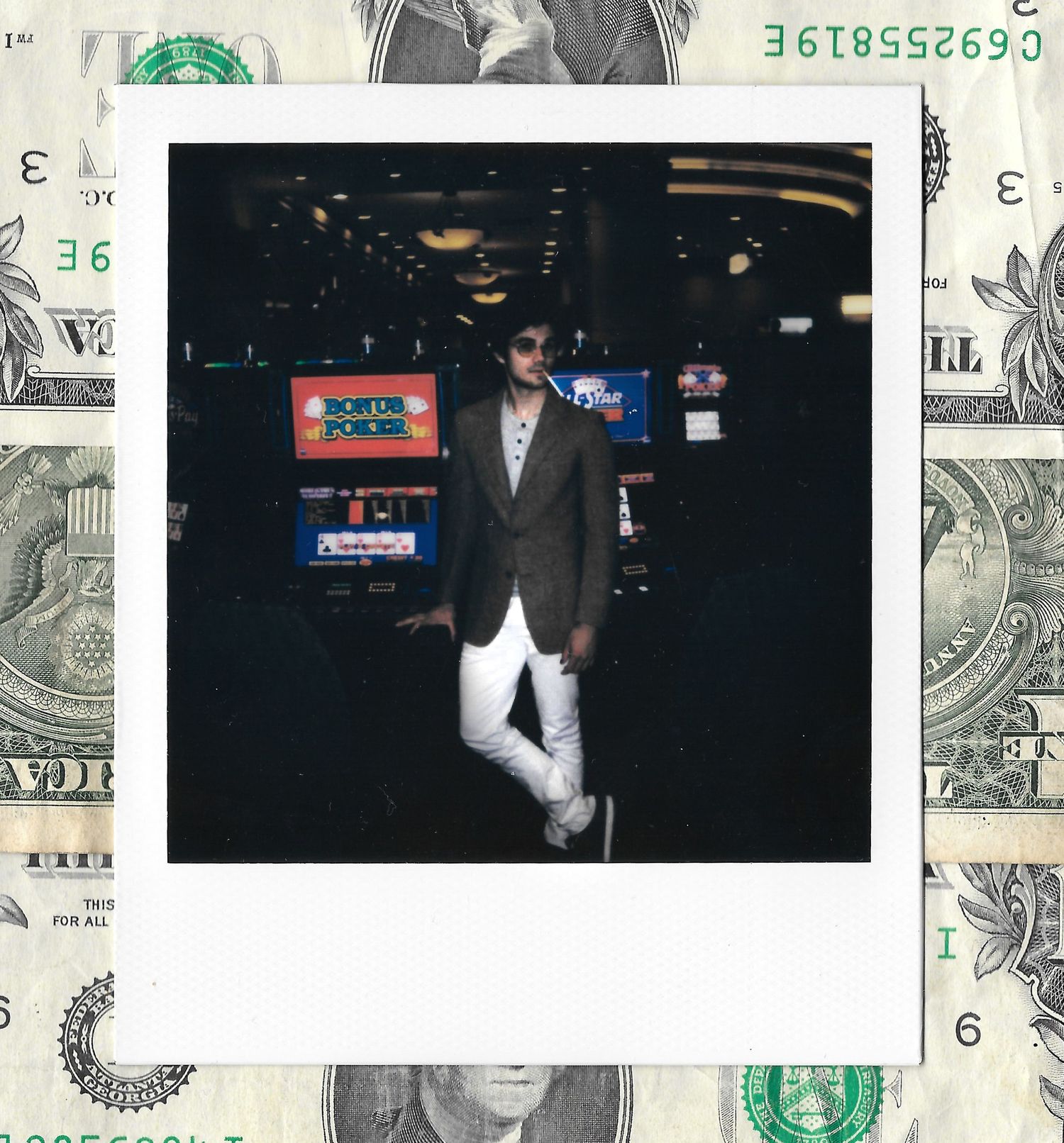 Man in brown blazer and white pants poses in a casino, framed by a Polaroid photo on a dollar bill background.