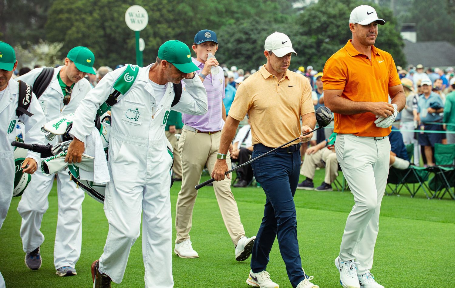 Golfers and caddies in green jackets walk the fairway at Augusta National during The Masters golf tournament.