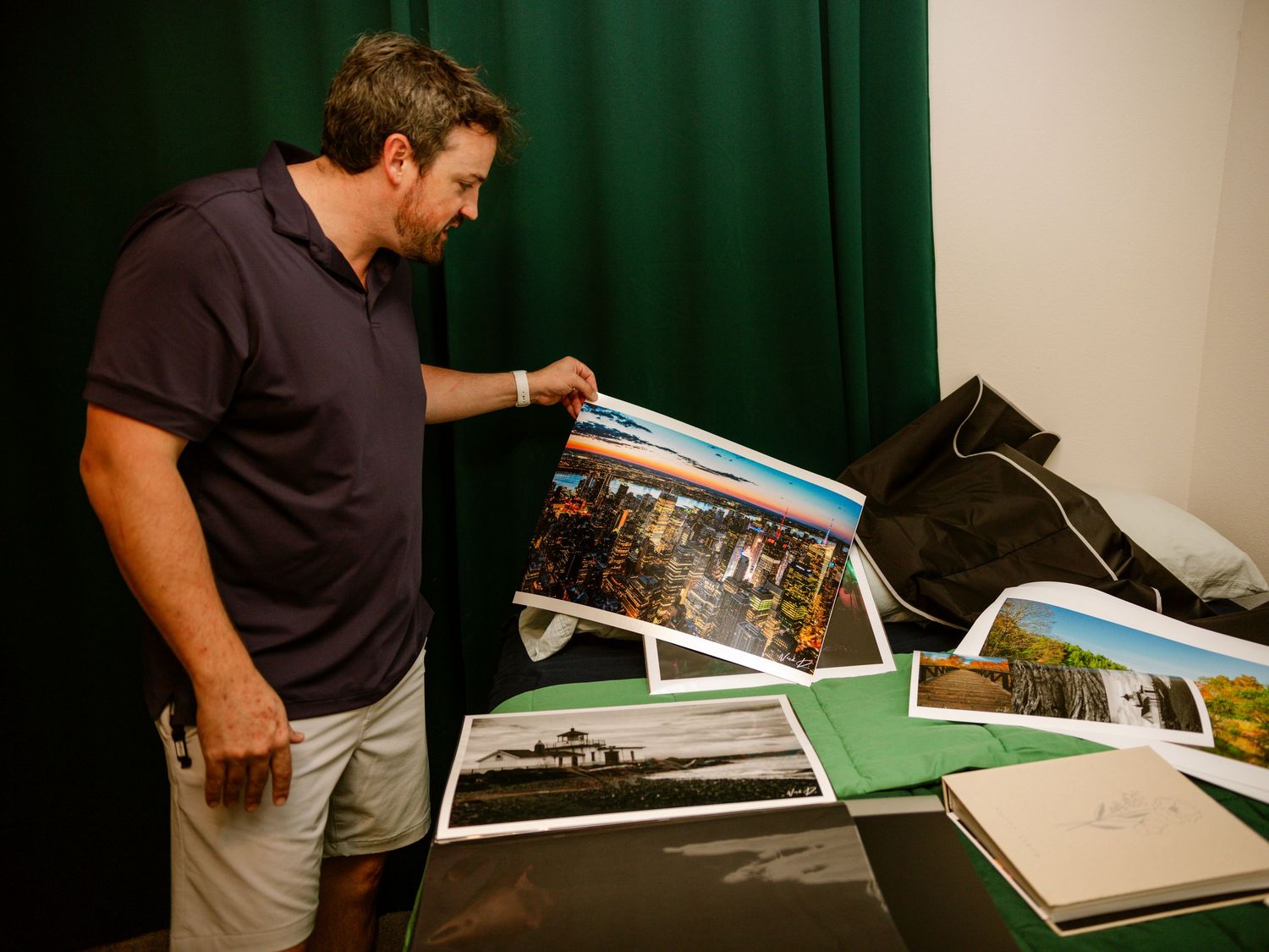 Man in navy polo reviewing large landscape photography prints on a green-draped display table.