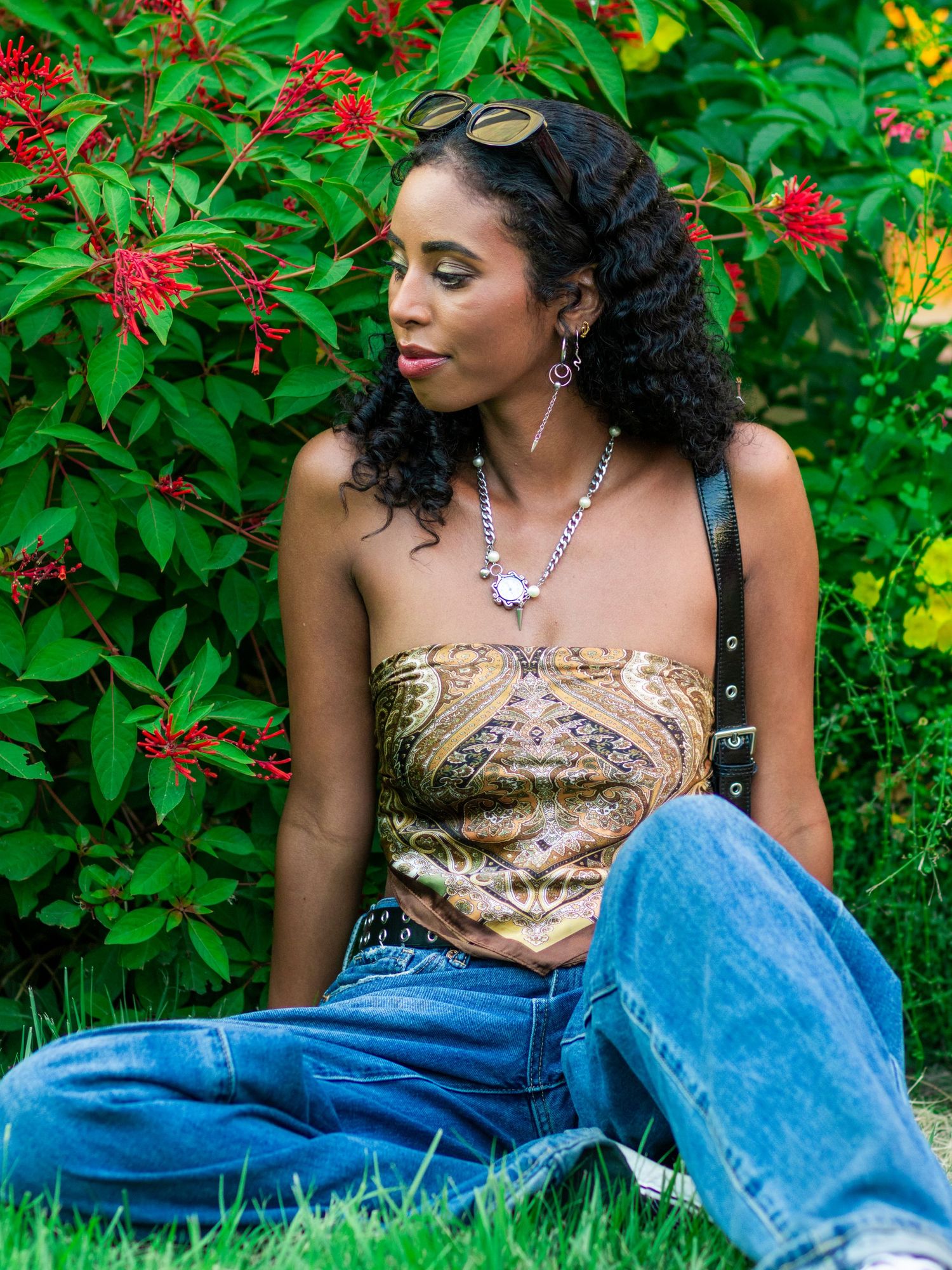Young Black woman with curly hair wearing a patterned strapless top and jeans in a garden.