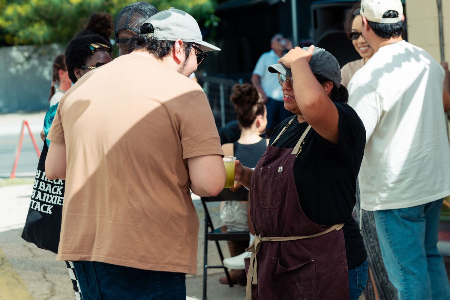 People gathered around a food vendor wearing an apron at an outdoor community event.