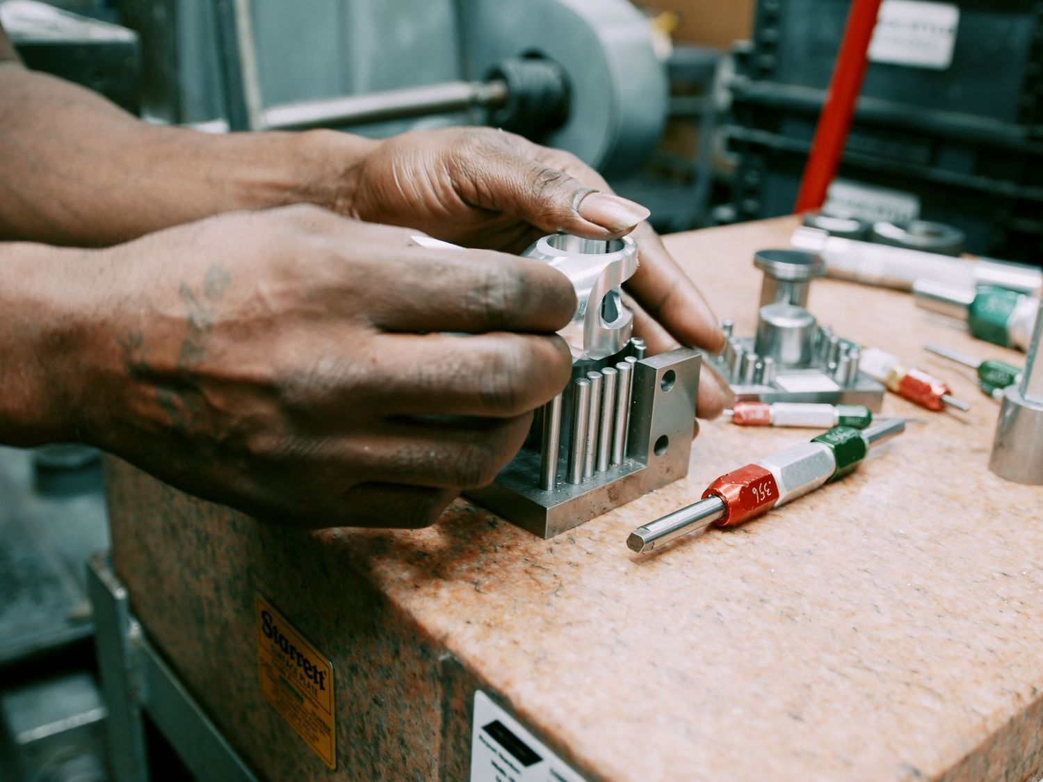 Worker assembles precision metal components on a workbench with tools nearby.