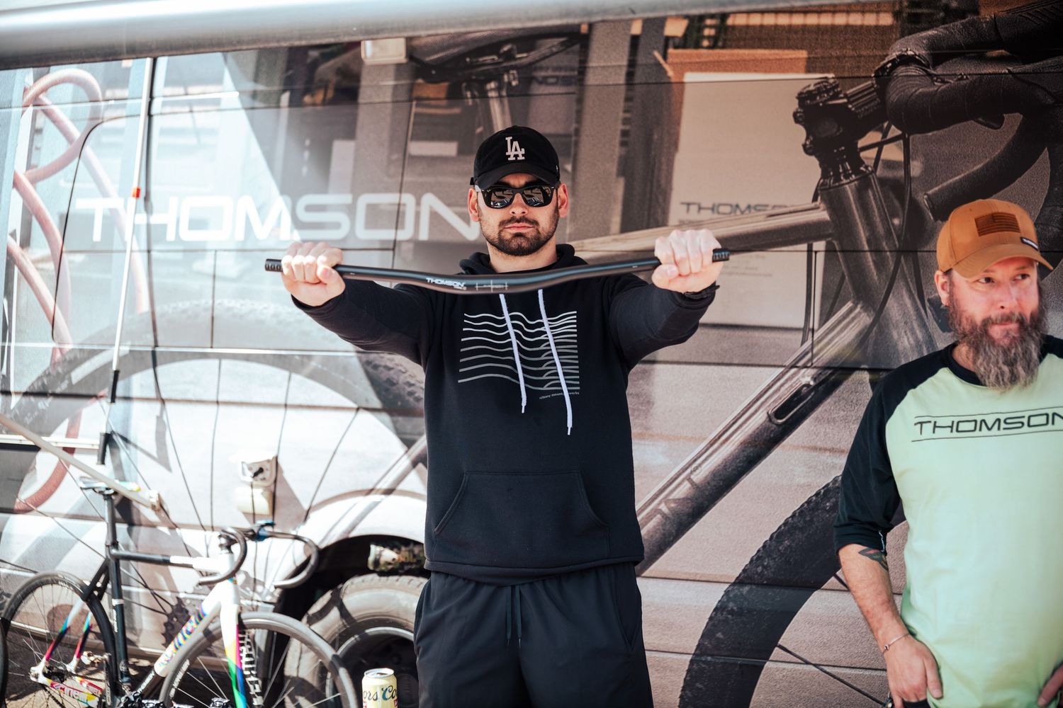 Two men at a Thomson bicycle trade show display, one holding a bike frame across his shoulders.