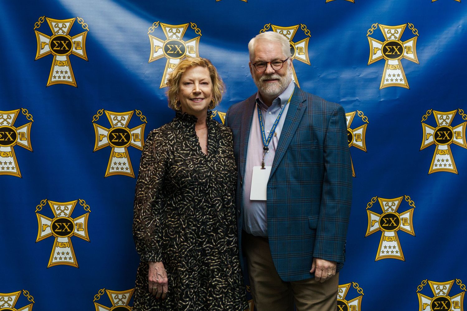 A man and woman pose together in front of a blue Sigma Nu fraternity banner at a formal event.