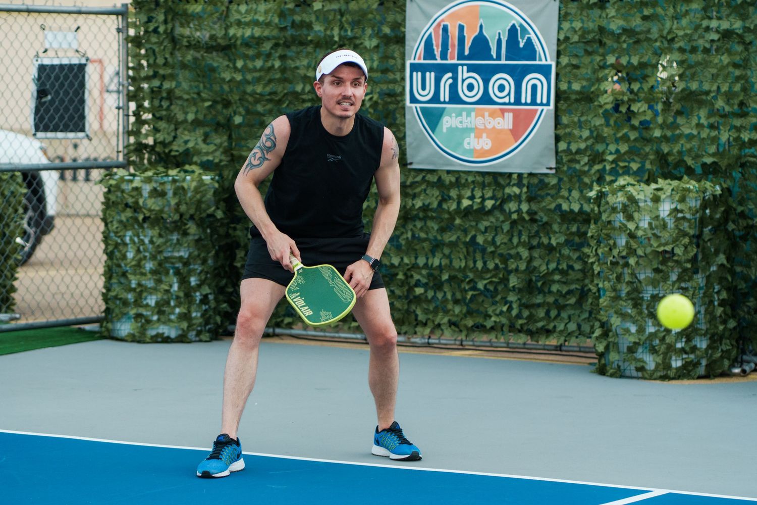 Man playing pickleball on blue court, holding green paddle, ready to return ball at Urban facility.