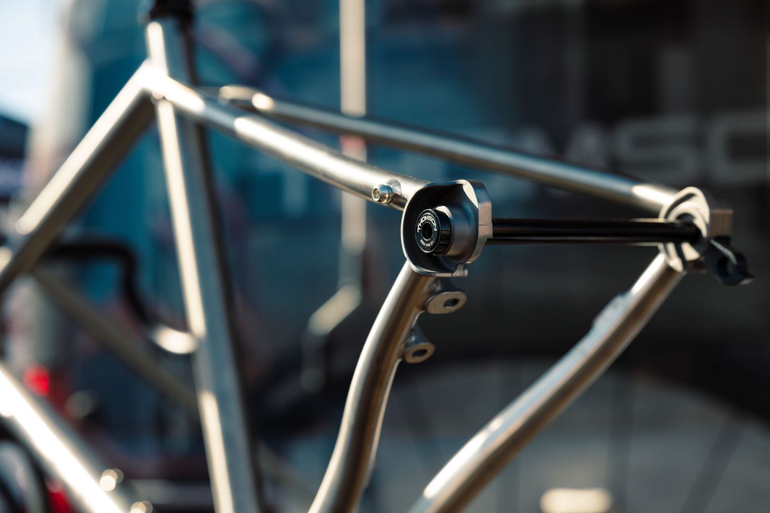 Macro shot of a titanium bicycle frame dropout with a black quick-release skewer in sunlight.