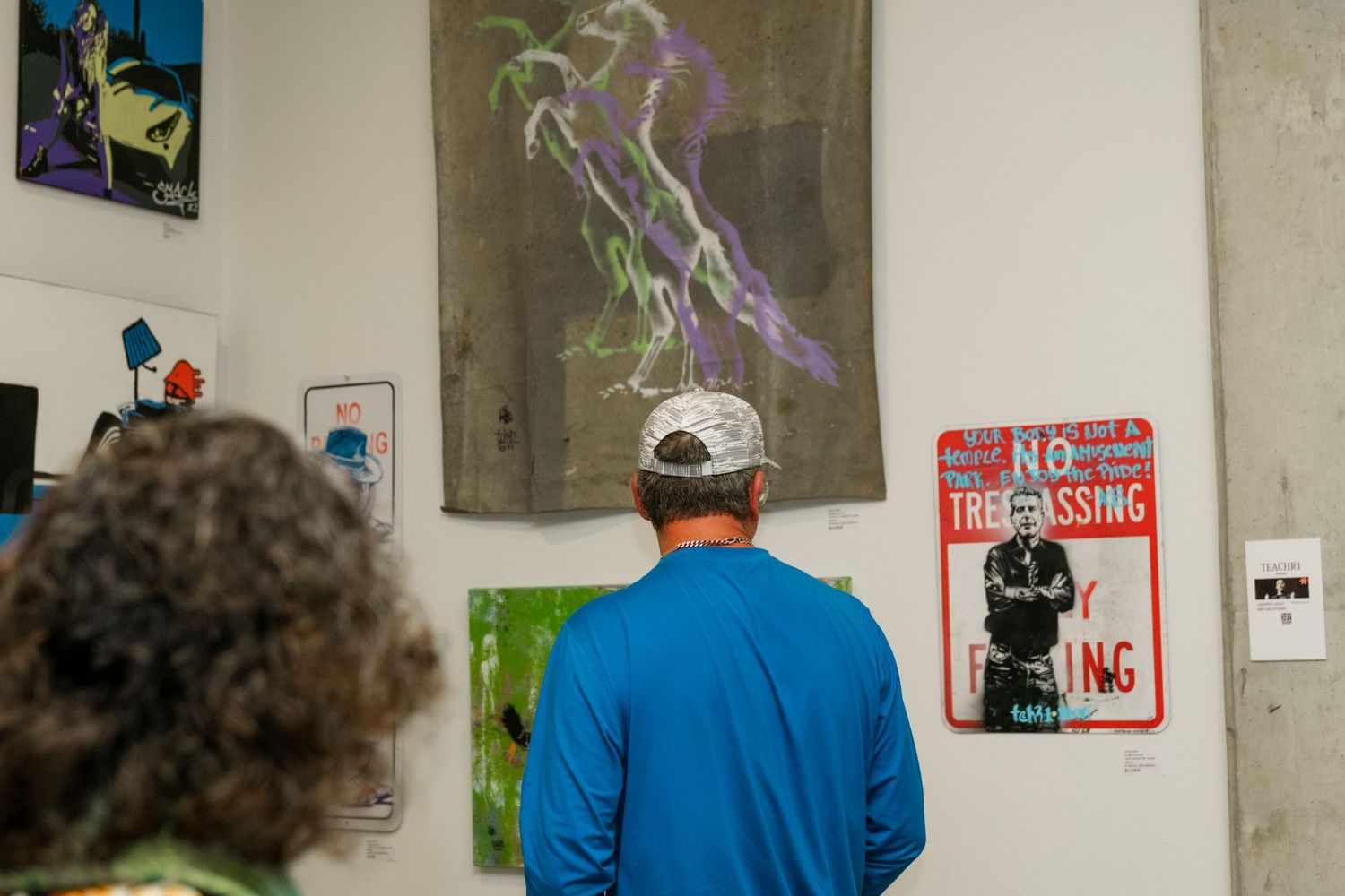 Man in blue shirt viewing abstract paintings at an indoor art gallery exhibition.