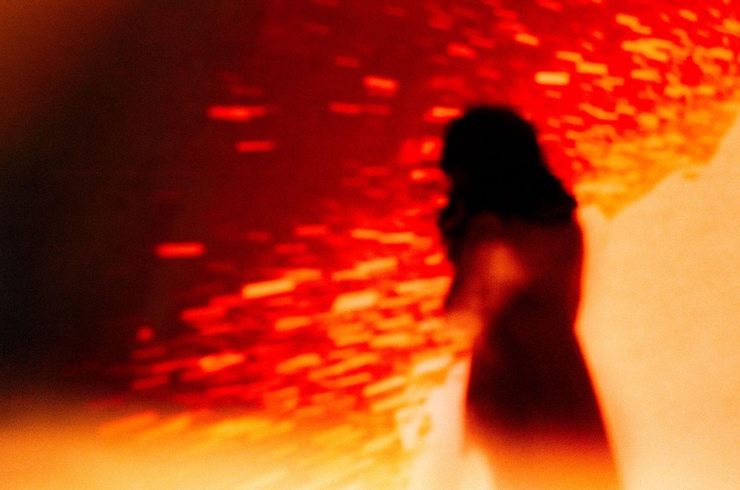 Blurred silhouette of a woman against a vivid red and orange glowing textured wall in artistic photography.