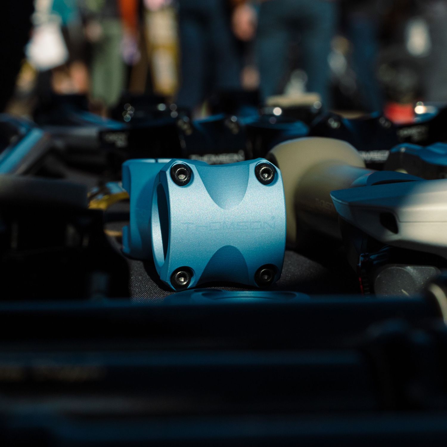 Close-up of a teal blue mountain bike stem with four bolts at an outdoor cycling expo.