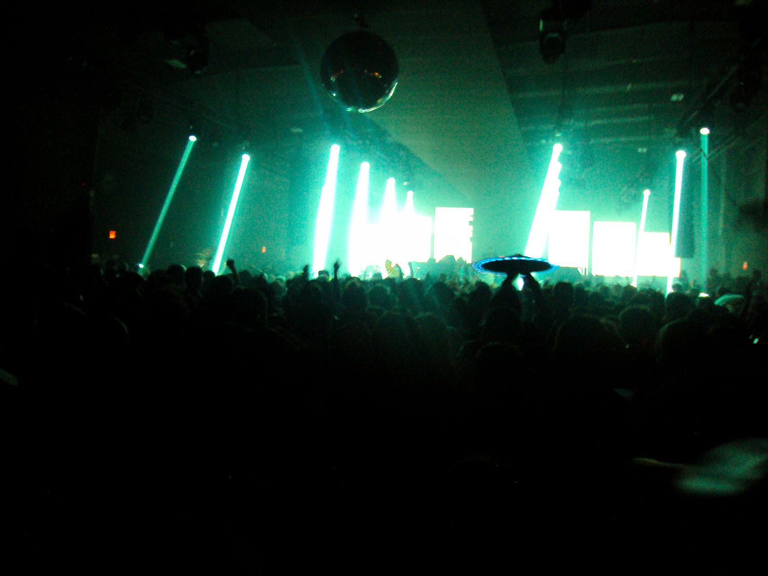 Crowded nightclub with green laser lights and a disco ball illuminating the dark dance floor.