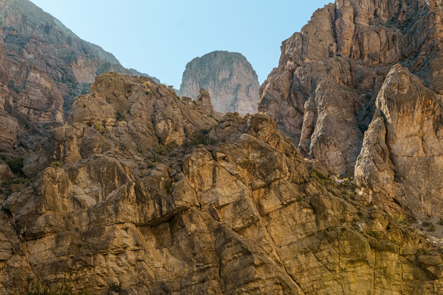 Rugged rocky mountain cliffs with towering stone formations under a clear blue sky in warm golden light.