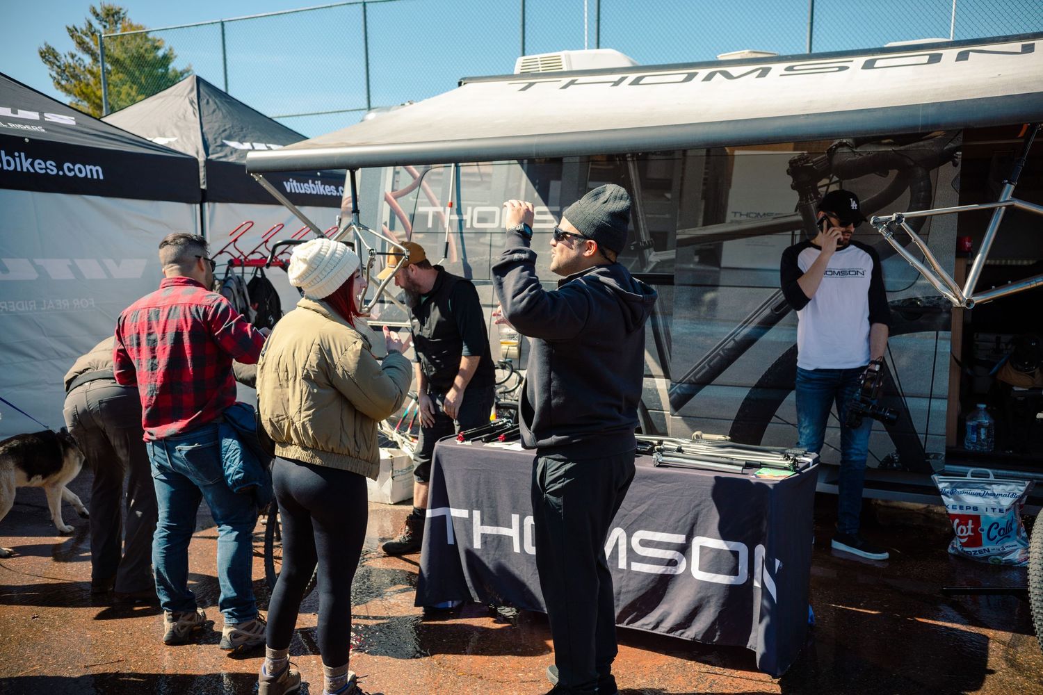 Cyclists gather at a Thomson bike components outdoor expo booth examining products on display.