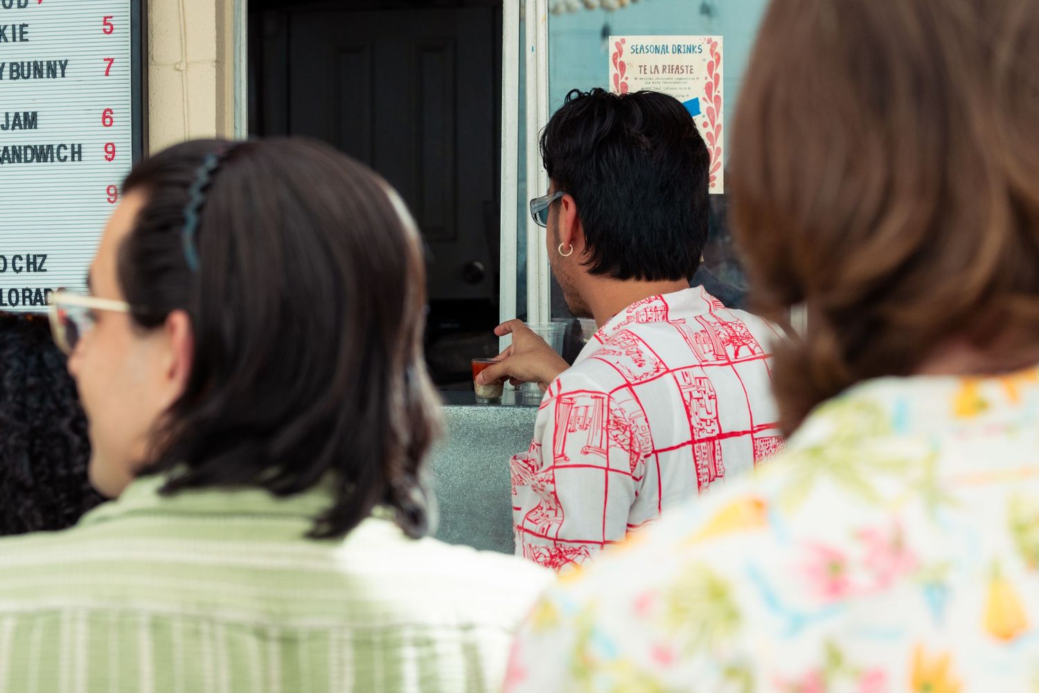 People standing in line at an outdoor food service window at a casual restaurant.