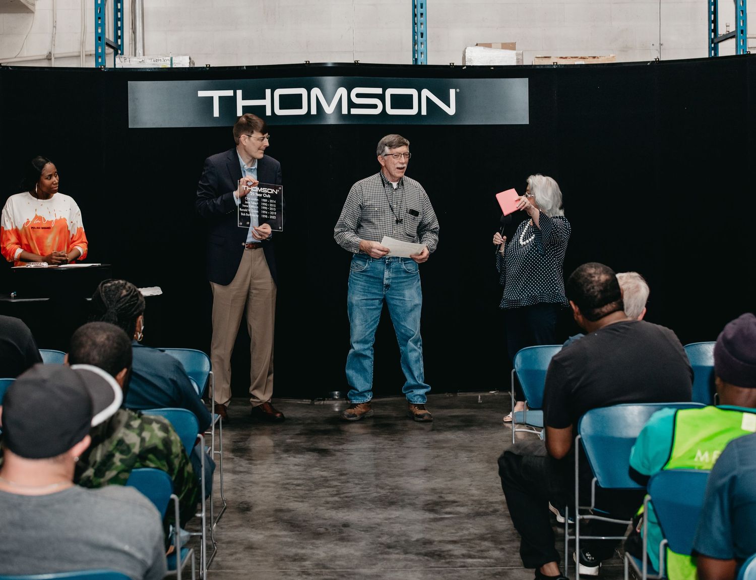 Award ceremony at Thomson facility with employees on stage receiving recognition before seated colleagues.