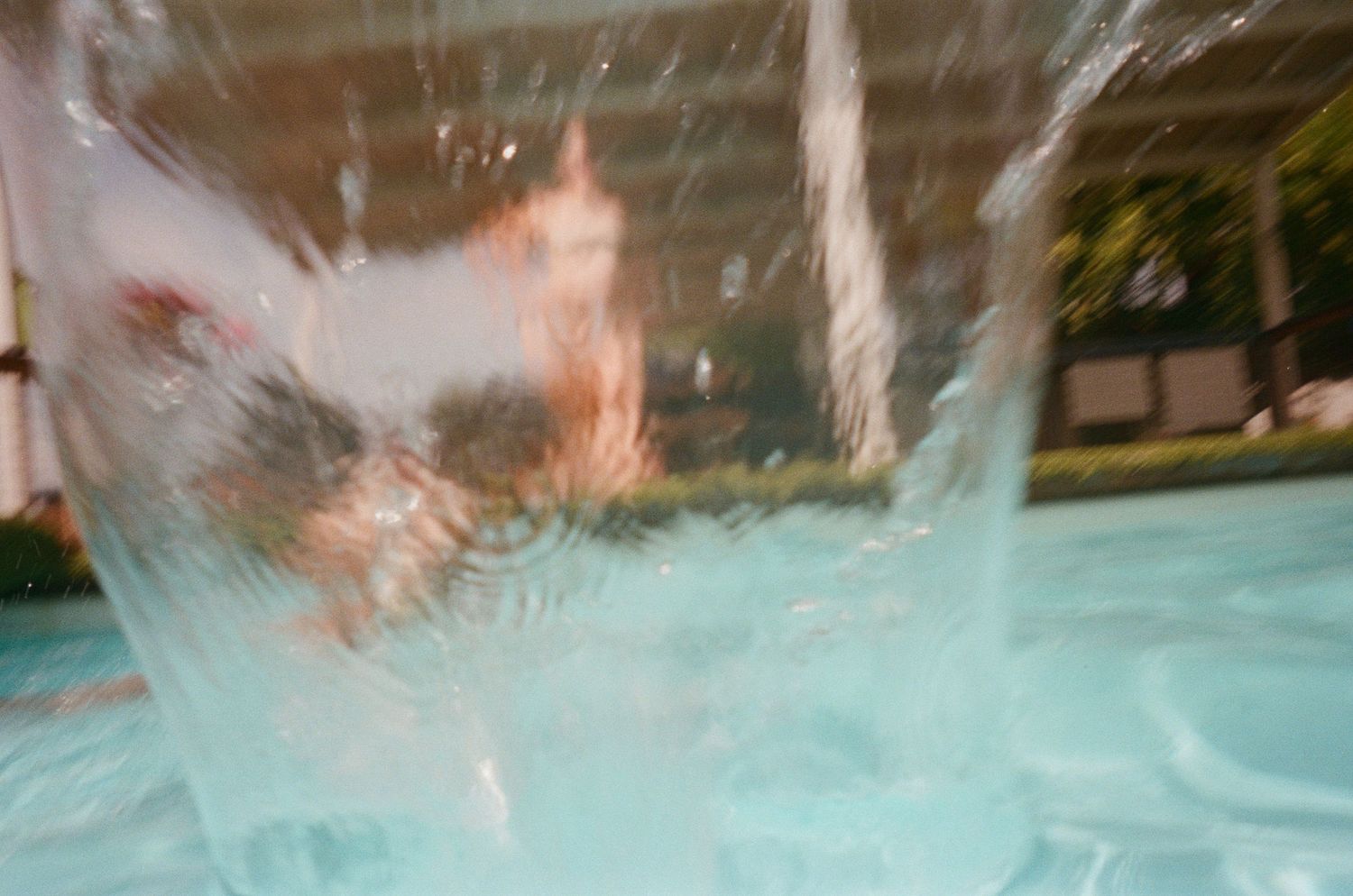 Person splashing into a bright turquoise swimming pool with water droplets frozen in motion.