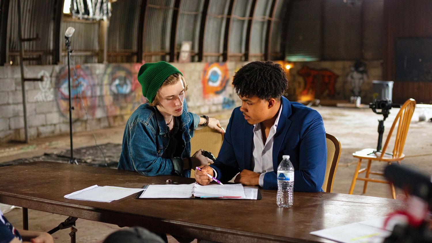 Two people collaborate at a table in an industrial space with graffiti walls, reviewing documents together.