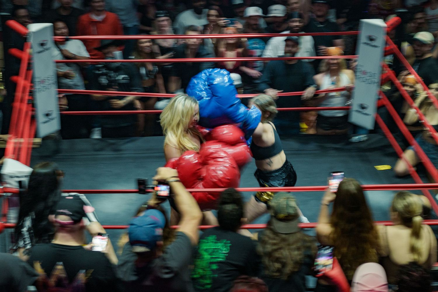 Two women in oversized red and blue boxing gloves clinch during an entertaining novelty boxing match.