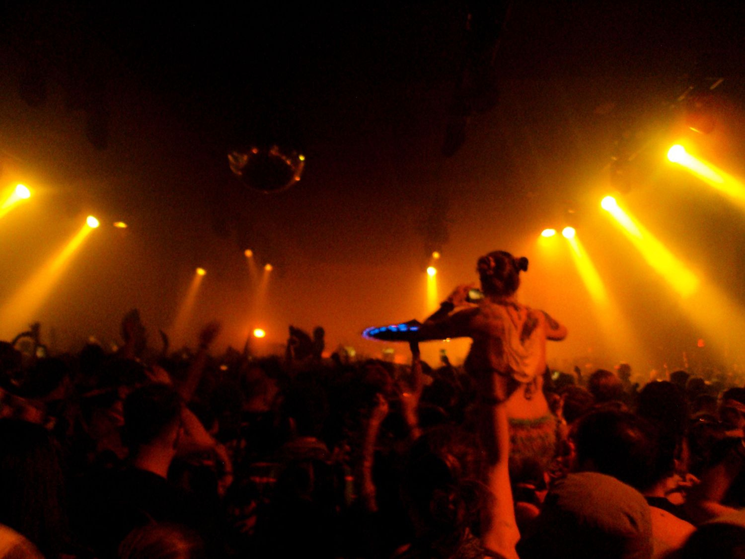 Crowd at a concert with yellow stage lights and a performer silhouetted against dramatic beams of light.
