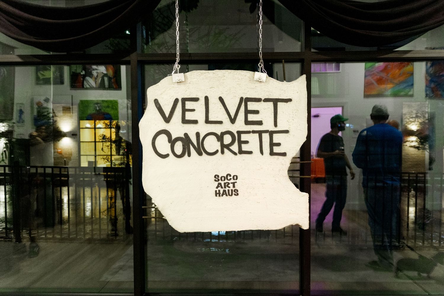 Velvet Concrete SoCo Art Haus exhibition sign displayed on glass gallery entrance doors at night.