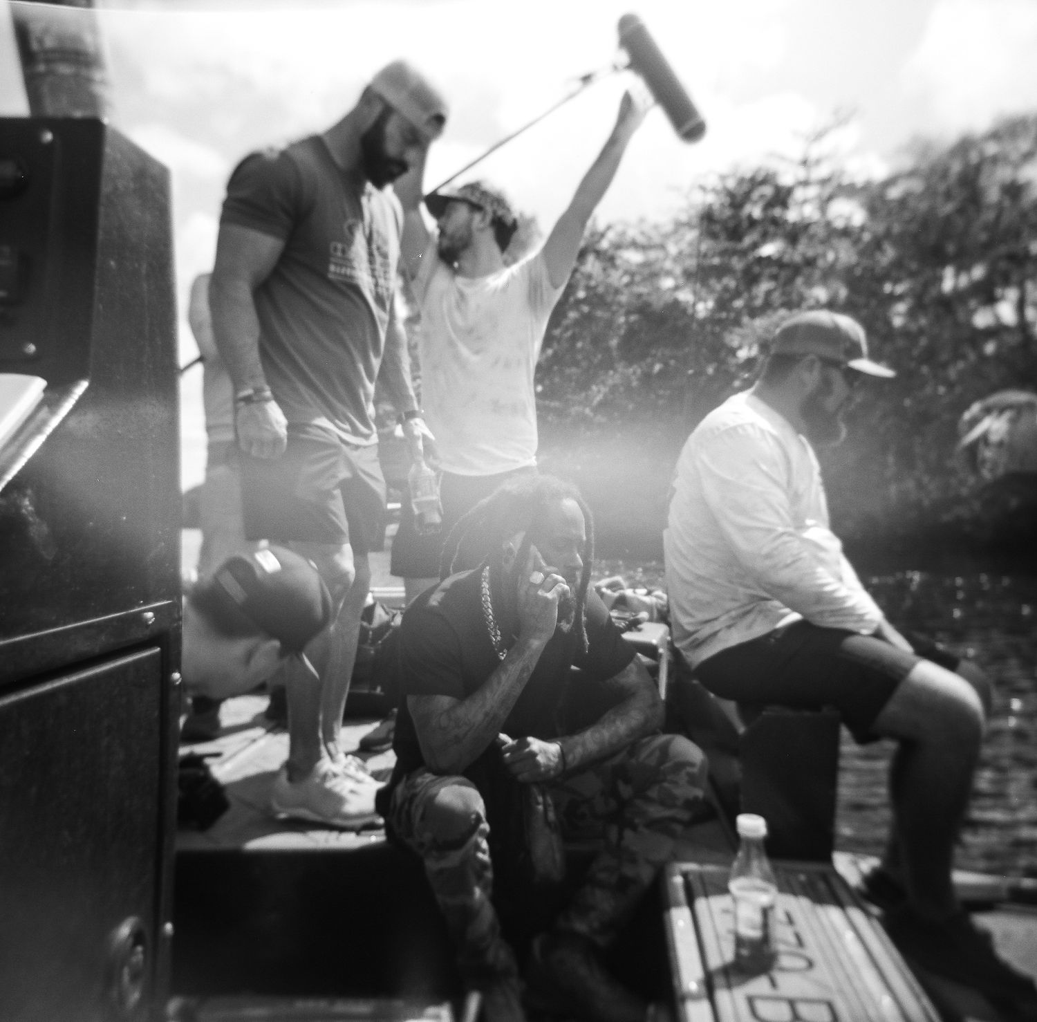 A film crew works on a boat with a boom mic raised, captured in dramatic black and white lighting.