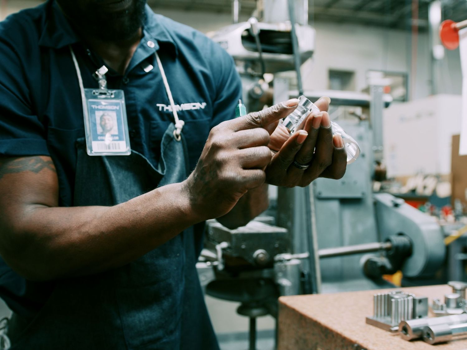 Factory technician inspects a small machined metal part in an industrial facility.