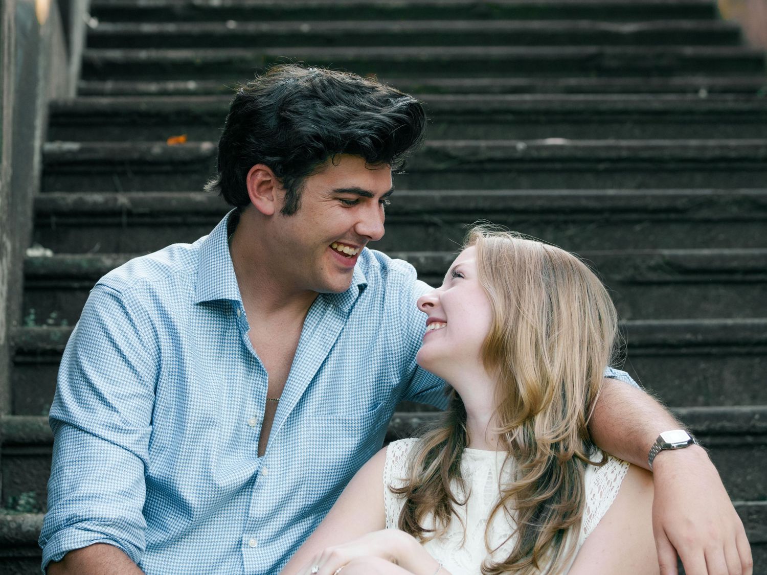 Happy couple sitting on stone steps smiling at each other in a candid outdoor portrait.