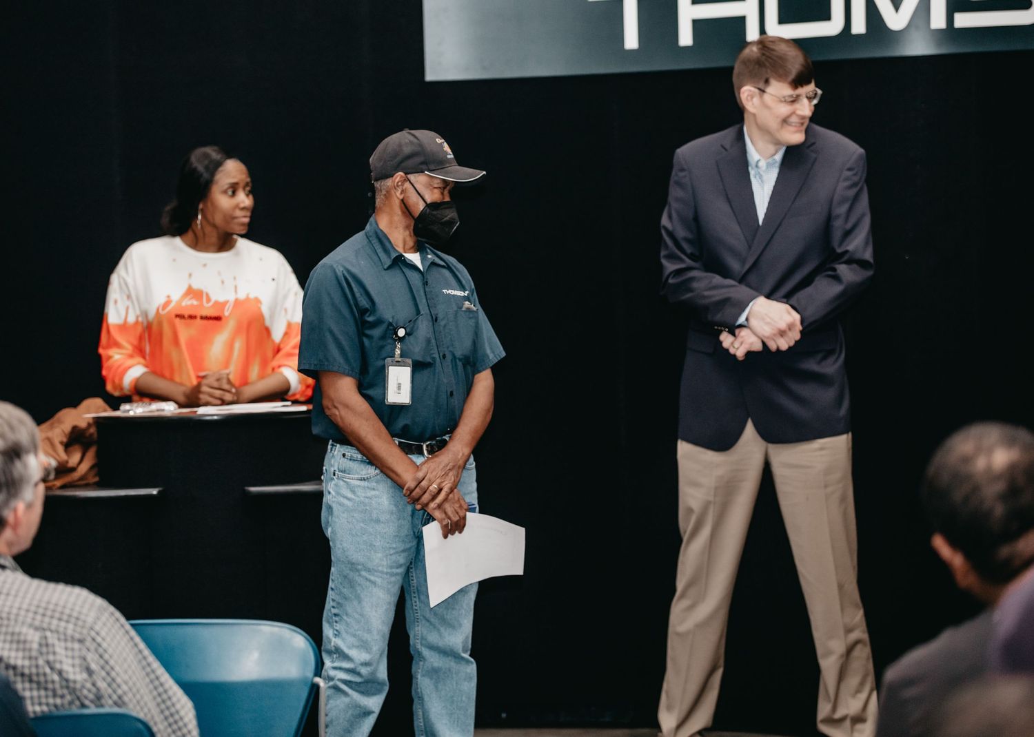 Three people standing on a stage during a professional presentation event in a modern venue.
