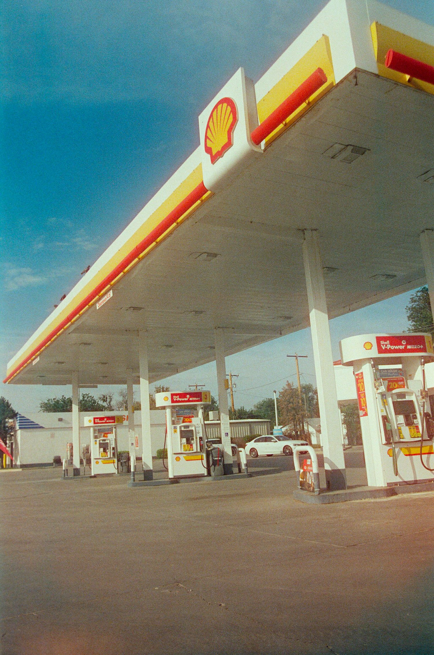 Shell gas station with multiple fuel pumps under a large white canopy with iconic red and yellow Shell logo.