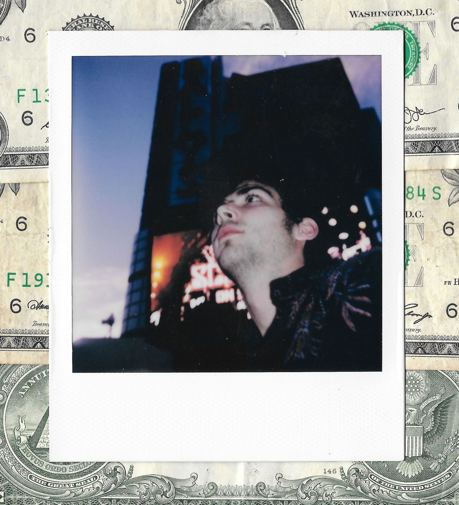 A young man gazes upward in a Polaroid photo, set against a backdrop of US dollar bills.