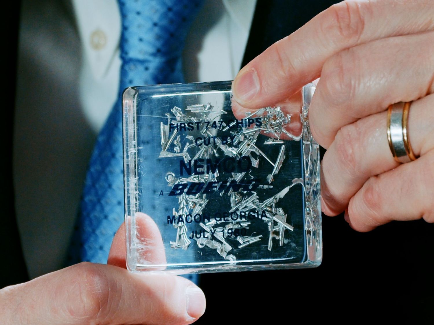 Person in suit holds transparent acrylic block with engraved signatures and text.