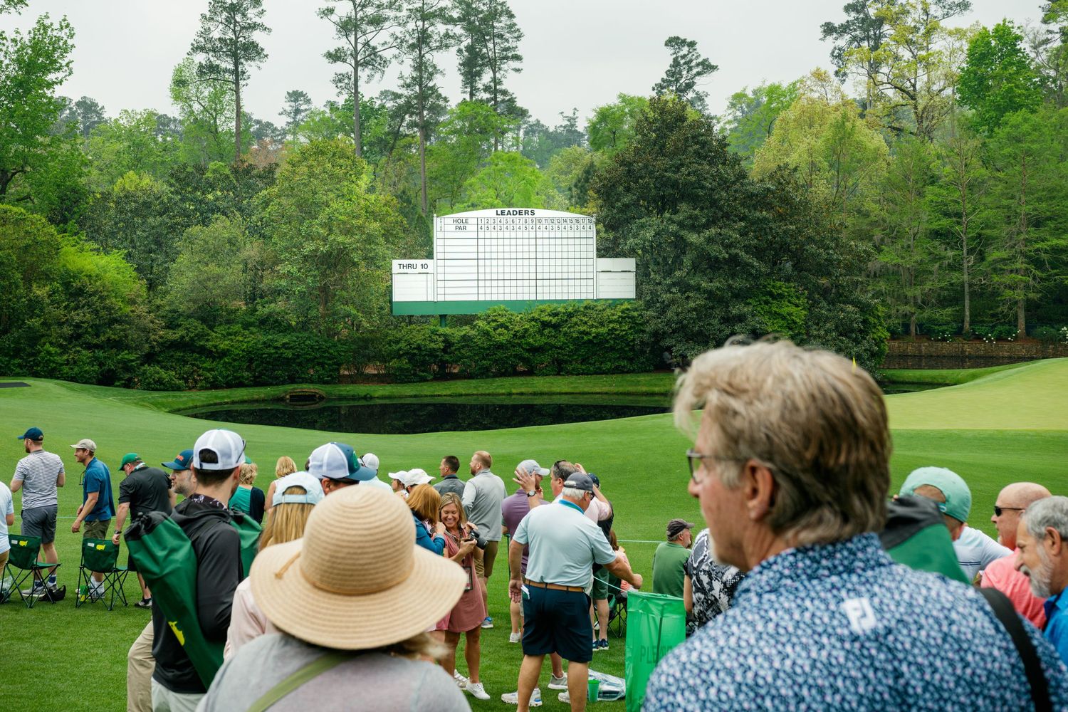 Crowds of spectators gather on a lush green fairway at Augusta National Golf Club during the Masters Tournament.