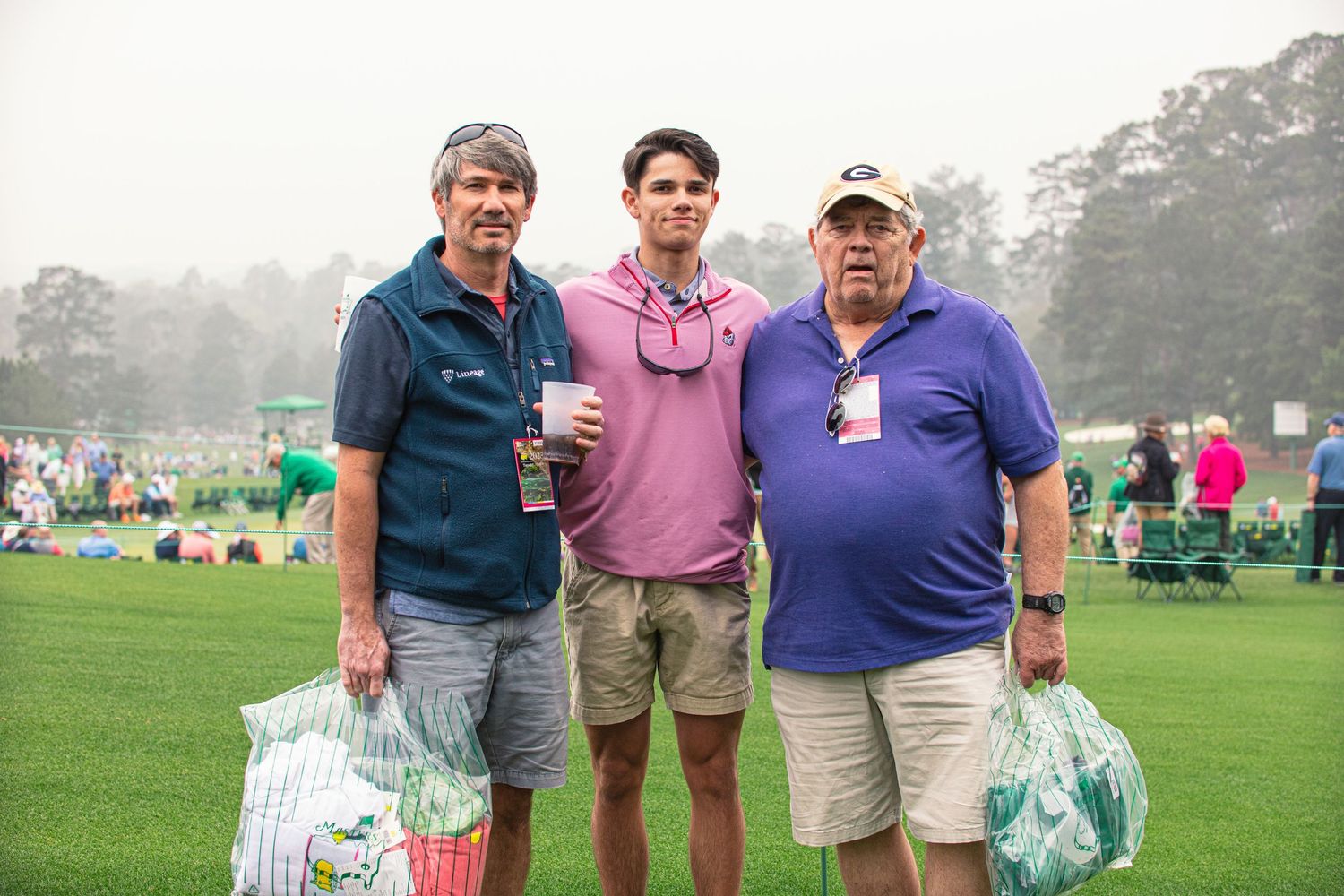 Three men posing together on a golf course at what appears to be a professional golf tournament.