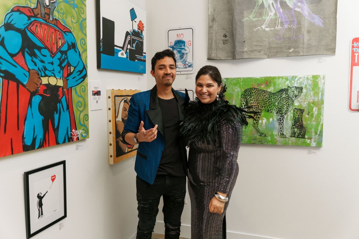 Two people smile together surrounded by vibrant pop art paintings at an art gallery opening.