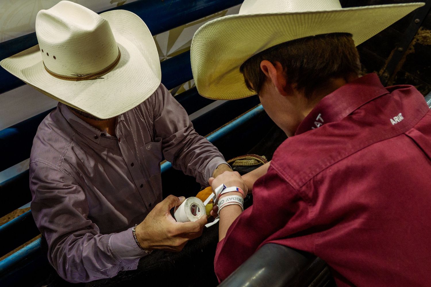 Two cowboys in white hats taping wrists before a rodeo event.