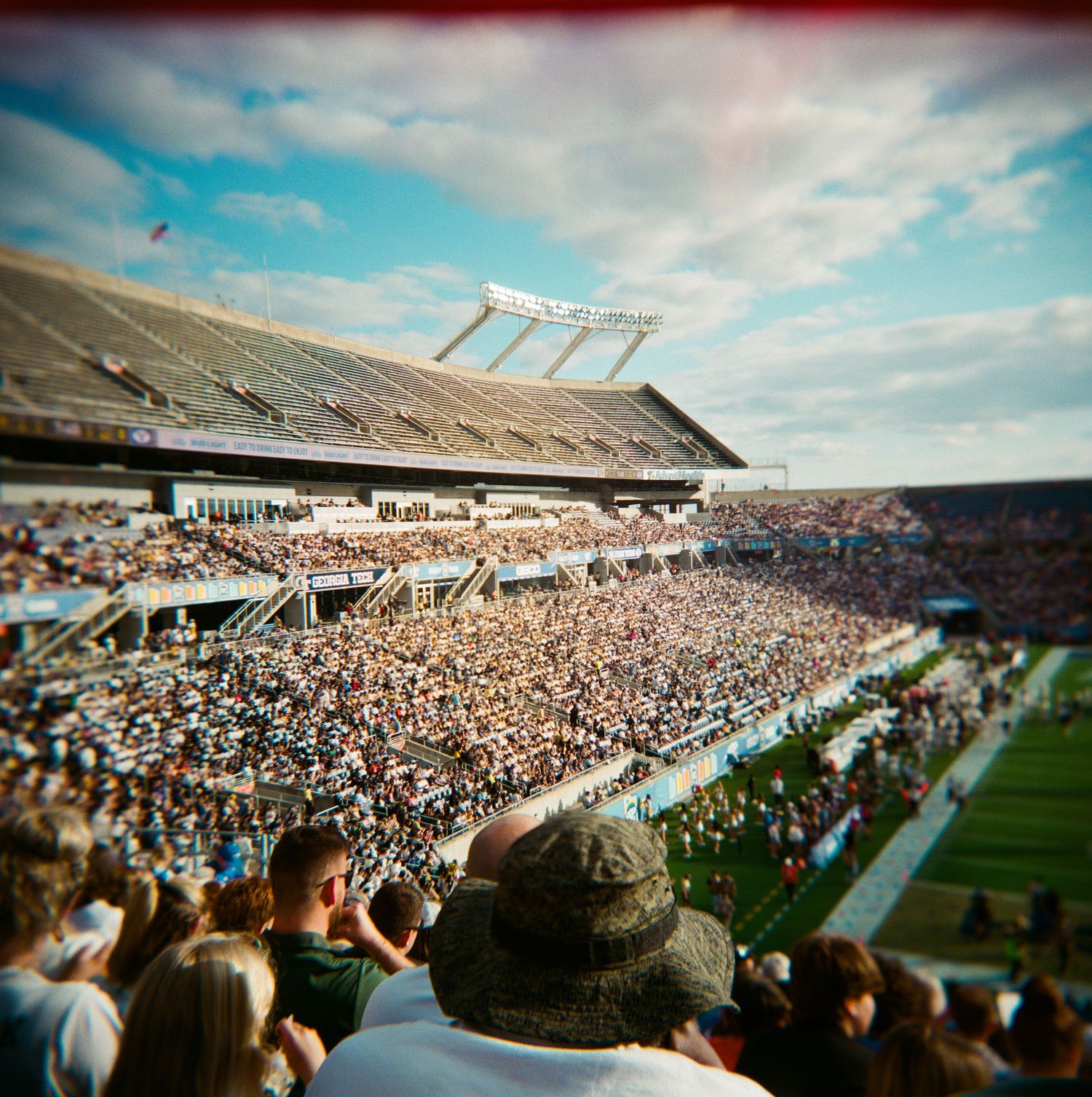 Wide angle film photo of massive crowd filling entire college football stadium on cloudy day.