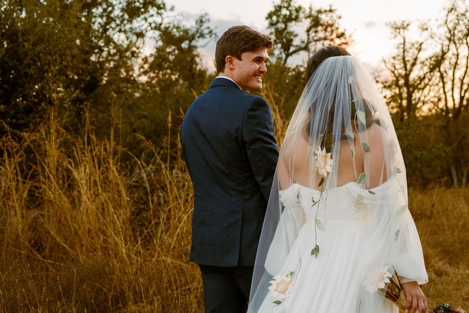 Bride and groom sharing a romantic moment in golden field at sunset, bride wearing white gown and veil.
