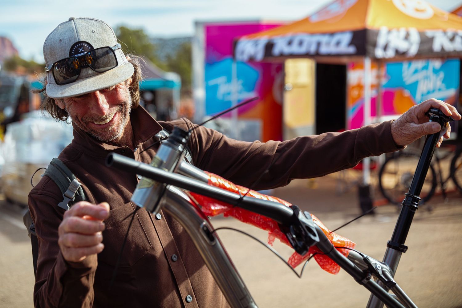 Smiling man holds a mountain bike handlebar at a colorful outdoor cycling event.