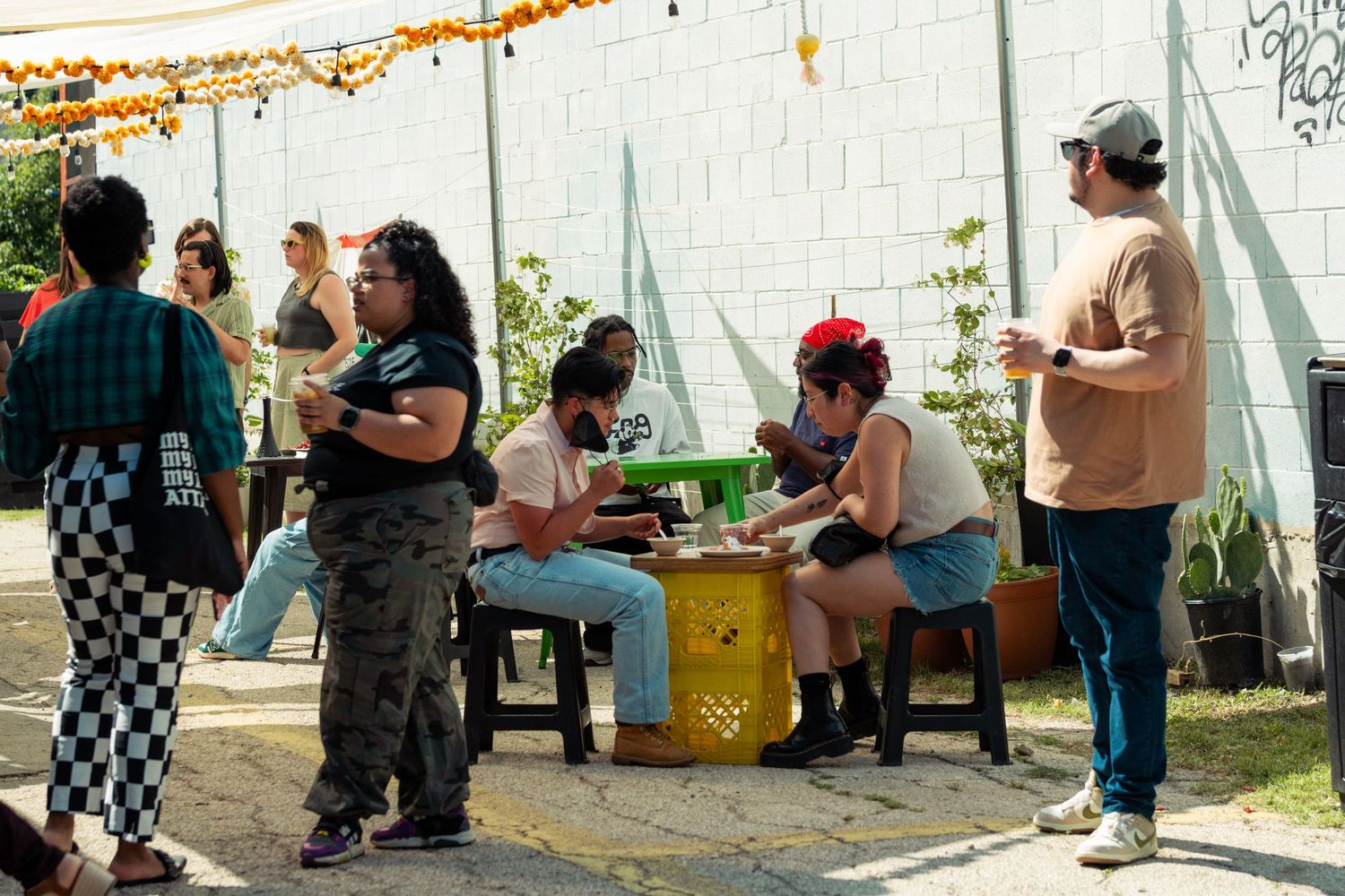 Group of people gathered outdoors at colorful tables during a casual street festival event.