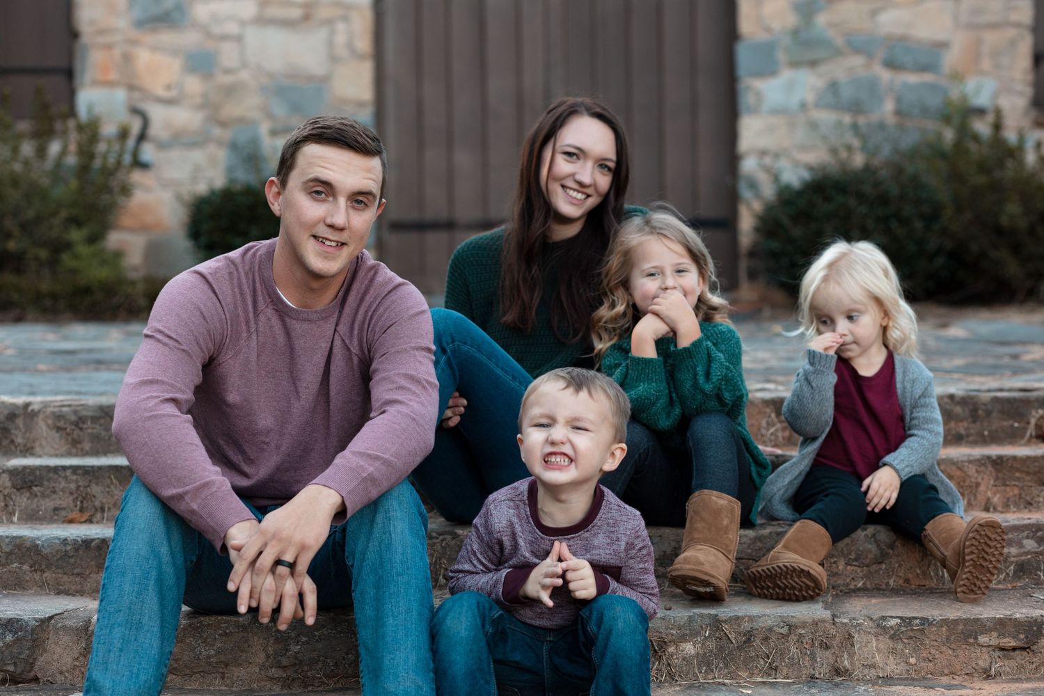 Family of five posing on stone steps, parents smiling with three young children.