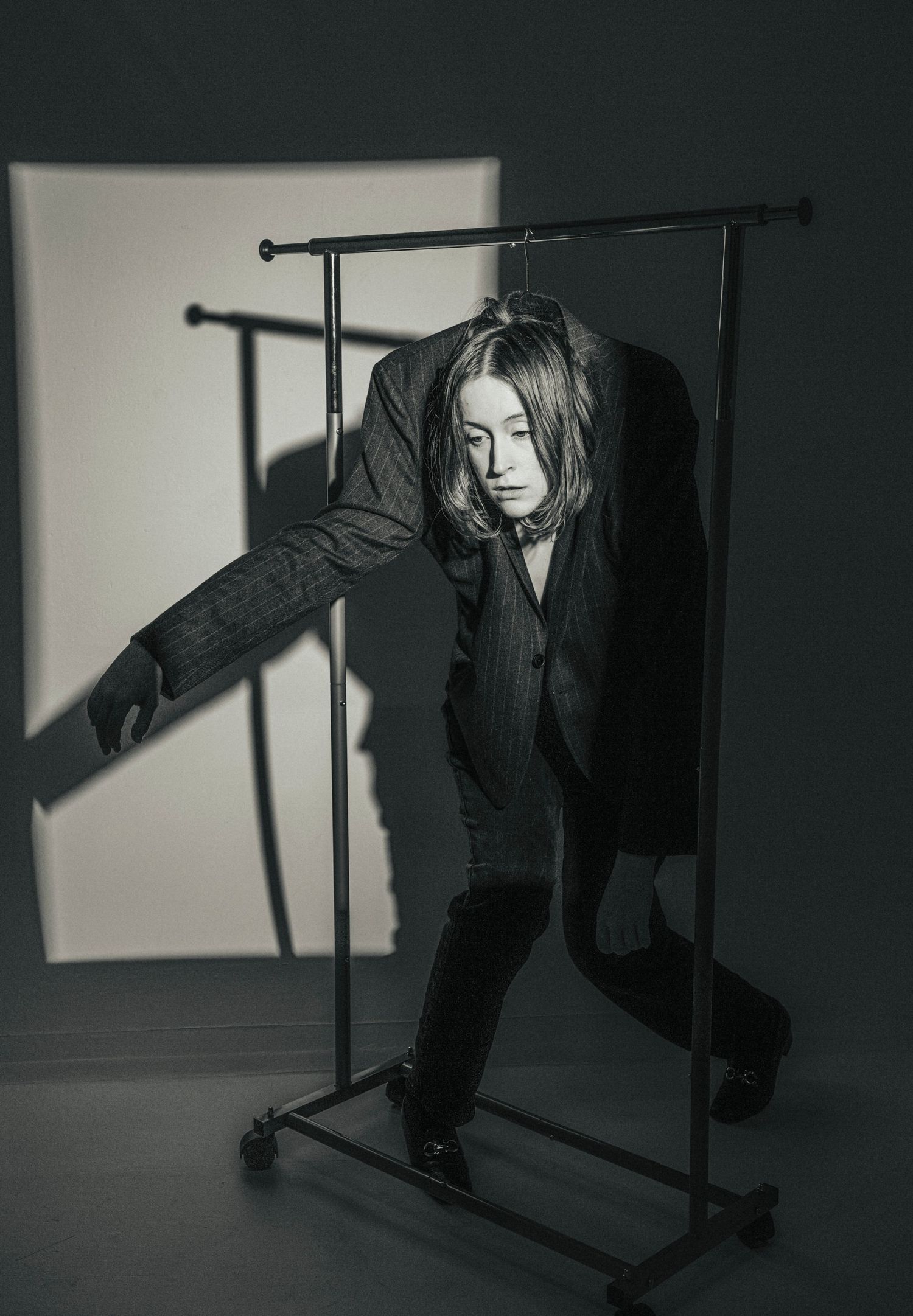 Black and white photo of person leaning through clothing rack in oversized pinstripe suit.