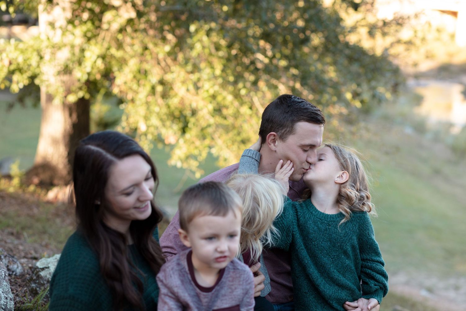 Parents kissing while three young children sit together outdoors in autumn setting.