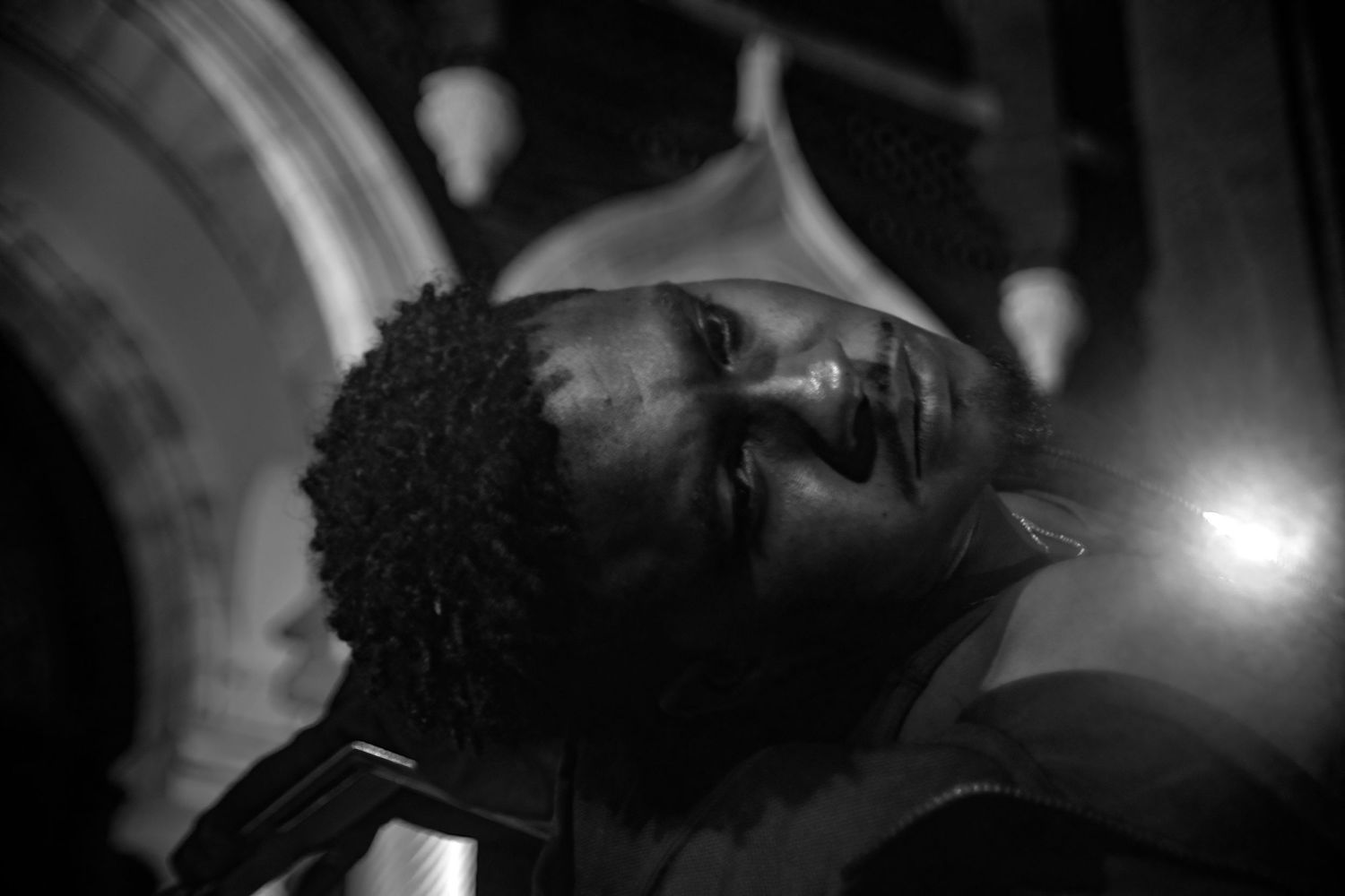 Black and white portrait of a young Black man looking upward, illuminated by dramatic side lighting.