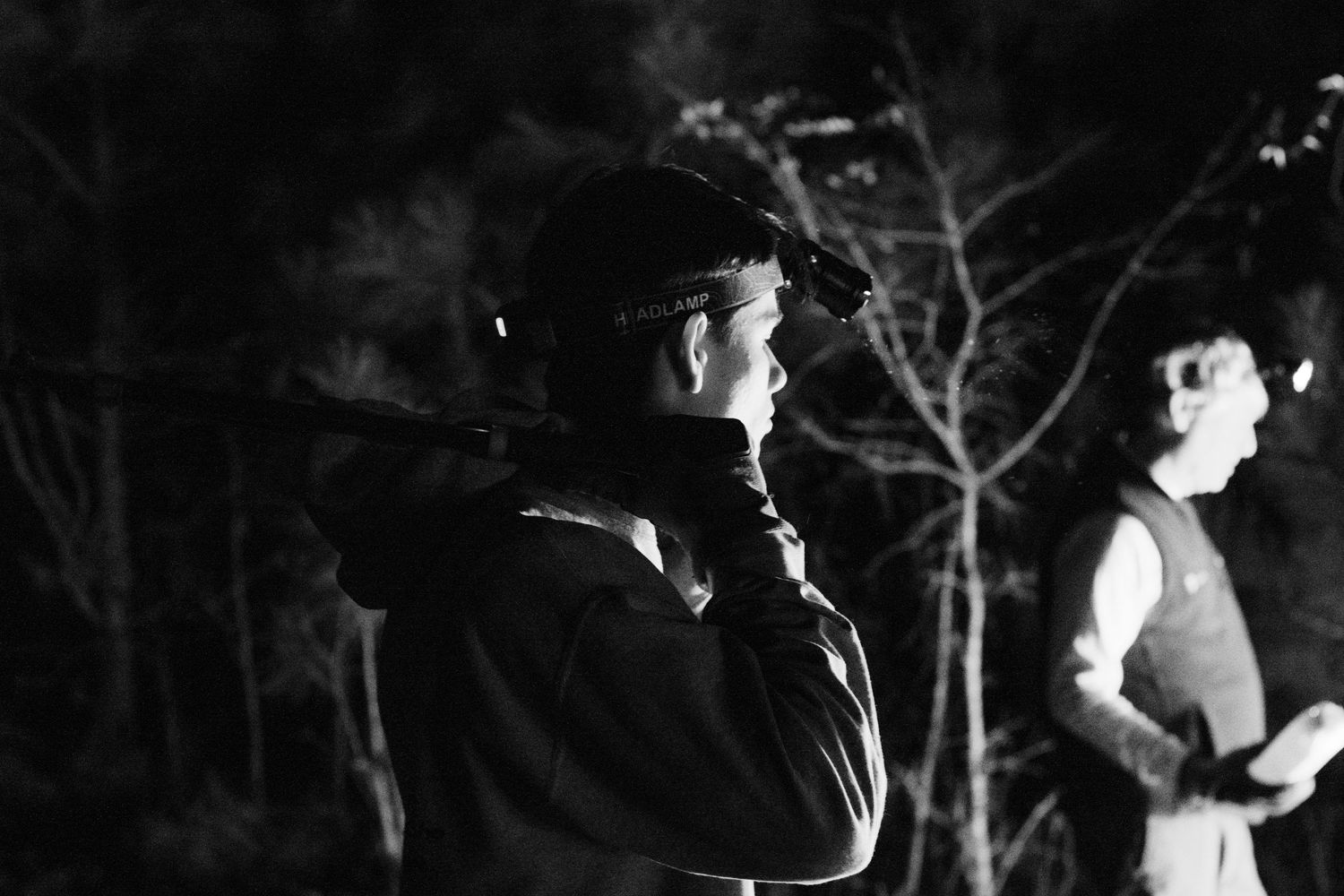 Black and white photo of person holding camera outdoors at night among trees.
